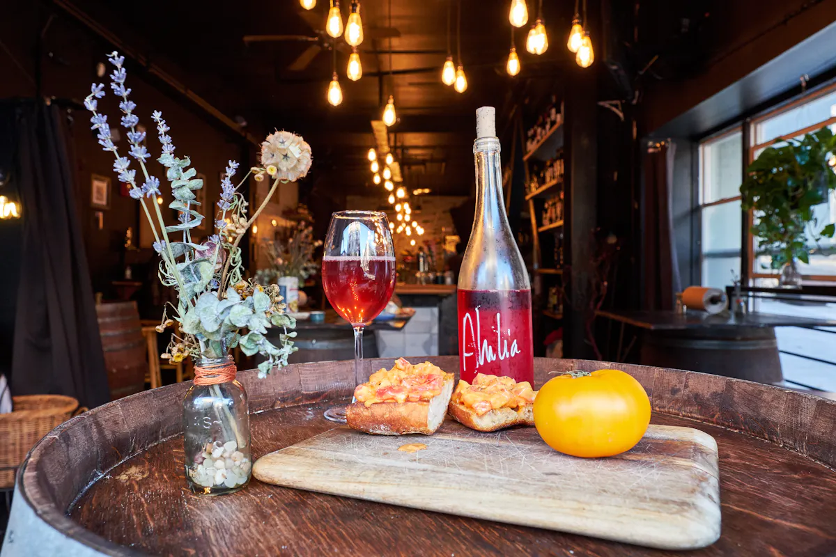 a bottle of red wine sitting on top of a wooden table with snacks and a glass